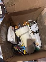 Top view of cardboard box with white food processor base, power cord, wooden bowls, and box of cooker liner.