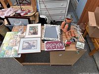 Clear image showing a collection of assorted decorative knickknacks including framed pictures, mirror, terracotta figurines, plaques, and glass items.