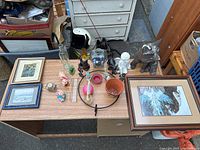 Top down photo of assorted knickknacks on a wooden table including framed artwork, glass bottles, figurines, candle holder, and planter.