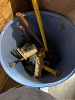 Blue plastic bin with assorted hand tools showing wooden and yellow handles including hammers and other metal tools