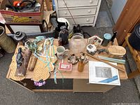 Top-down photo of a table displaying an assortment of knickknacks including figurines, glass jars, framed art pieces, tapes, wooden kitchen utensils, and more.