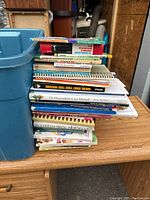 Stack of assorted nature and gardening books on table with blue storage bin beside.