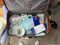Top-down view of a suitcase containing assorted crystal pieces, candle holders, boxed candles, incense sticks, and fabric cloths.