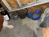 Photo showing four different ceramic figures on floor including a small round vessel, green pot, blue/brown bird, and a white rough human-shaped figure