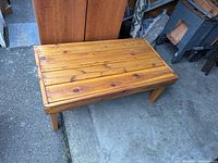 Photo showing the top and one side of the wooden coffee table placed outdoors, highlighting natural wood grain and plank construction.