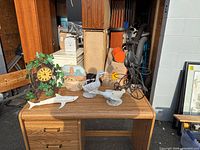 Wide photo showing assorted decorative display items atop a wood grain desk with drawers, including animal figurines, a clock, and a tricycle item.