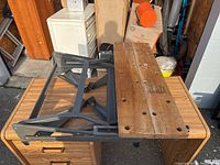 Foldable work table showing wooden top and black foldable legs, viewed from the side and angled from above.
