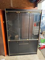 Full front view of the black glass display unit showing glass doors, gold hinges, and lower cupboards.