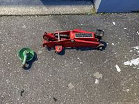 Photo showing a red hydraulic car jack and a green snatch block on pavement surface