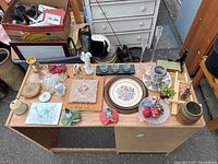 Wide view of assorted knickknacks on a wooden cabinet, showing many figurines, plates, glass items and small decorative pieces.