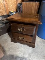 Two matching wooden bedside tables with two drawers each, brass handles, and some wear visible on surfaces.
