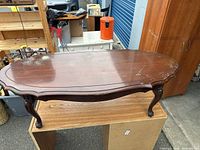 Photo of the mid-century modern wooden coffee table showing the scalloped top with wear marks and carved cabriole legs.