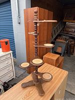 Front angled view of mid-century modern wood plant stand with turned central column, seven oval and round shelves with cane inlays and three-legged base.