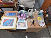 Top-down image showing various glass, ceramic, and framed art knickknacks arranged on a wooden cabinet