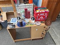 Overview of knickknacks on wooden table including figurines, candles, framed art, crate of papers, coasters and decorative items
