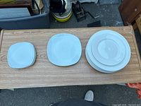 All six plates arranged on a wooden surface: two small square, two medium square, and two large round plates with decorative rims