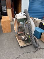 Dust collector unit showing metal hopper, cloth dust bag, motor and flexible hose on wooden base.