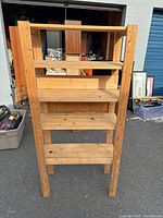 Front view of the wooden shelf showing five tiers made of wood planks and plywood back panel on middle shelf.