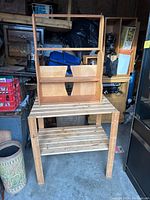 Photo of wooden wall-mounted shelf with two small compartments and an open shelf above, light colored wood, standing on a table in garage setting