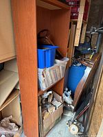 Wooden shelving unit with a blue plastic bin and clear bin containing papers or magazines on shelves, located in storage space.
