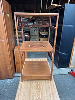 Front view of mid-century modern wooden side table with three shelves, showing removable tray shelf with handle and angled support beams on the sides.
