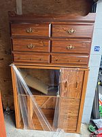 Photo showing wooden dresser with six drawers stacked on top of the TV unit, visible brass handles and wood grain.