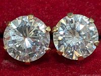 Close-up front view of the pair of stud earrings with round clear cubic zirconia stones set in 10K yellow gold prong settings on a red background.