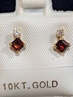 Pair of garnet and diamond stud earrings set in 10K gold with textured display card marked '10KT. GOLD'.