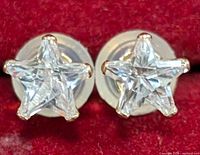 Close-up image of star-shaped earrings made from 9K gold with clear cubic zirconia stones on red background.