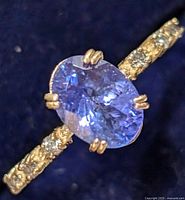 Close-up of oval violet-blue faceted tanzanite center stone with diamond-accented band on dark background