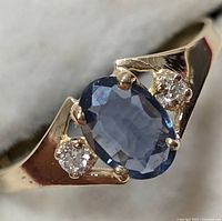 Front view of ring showing oval mixed cut blue sapphire center flanked by two round brilliant diamonds