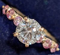 Close-up of central round brilliant diamond and pink accent stones on blue background