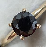 Close-up top view of round black diamond in six-prong setting on gold band.