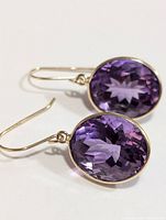 Pair of oval faceted amethyst gemstone earrings set in 10K yellow gold with drop hooks.