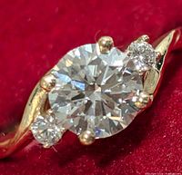 Close-up of central round brilliant diamond and side stones on red background