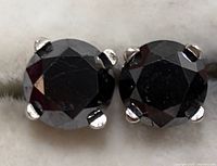 Front view of pair of black diamond stud earrings showing faceted stones in four-prong settings