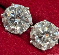 Front view of both stud earrings on red velvet background showing round brilliant diamonds in six-prong settings