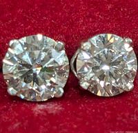 Close-up of two round brilliant lab-grown diamonds in four-prong white gold settings on red fabric background