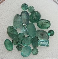 Top view of 20 loose genuine emerald gemstones showing variety of shapes and green hues
