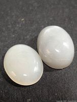 Two oval polished moonstones on a black background showing translucent white and grey colors.