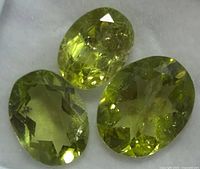 Close up of three oval faceted peridot gemstones showing internal facets and yellow-green color.