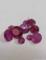 Close-up photo of eight genuine loose ruby gemstones varying in shape, size, and color on a white background.