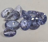 Loose faceted tanzanite stones arranged on a surface, showing various cuts and light violet-blue color.