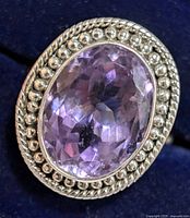 Close-up of the silver ring with an oval faceted amethyst stone, showing intricate beaded detailing around the stone.