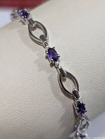 Close-up of silver and amethyst bracelet segment showing oval amethyst gemstone set in four-prong setting connected to an open silver link.