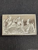 Front side of silver bar showing engraved scene of soldiers on horseback in ceremonial uniform.