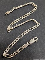 Close-up of the silver link chain bracelet showing the lobster clasp and link design on a black background.