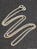 Overall view of the silver chain necklace laid out with visible curb links and spring ring clasp.