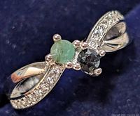 Close-up of silver ring with emerald, sapphire, and small clear stones on twisted band, showing frontal and side views