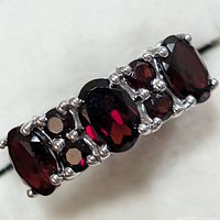 Close-up front view of silver ring with five oval garnet stones showing deep red color and prong settings